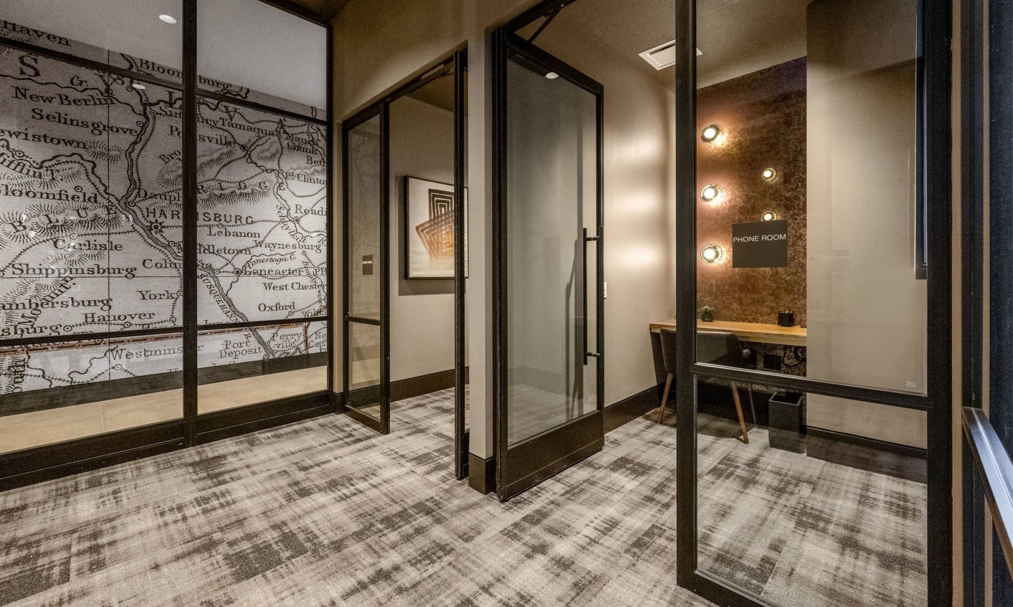 Madison West Elm apartments Modern office space with glass walls, a map mural, and a small phone room with a desk and wall lights.