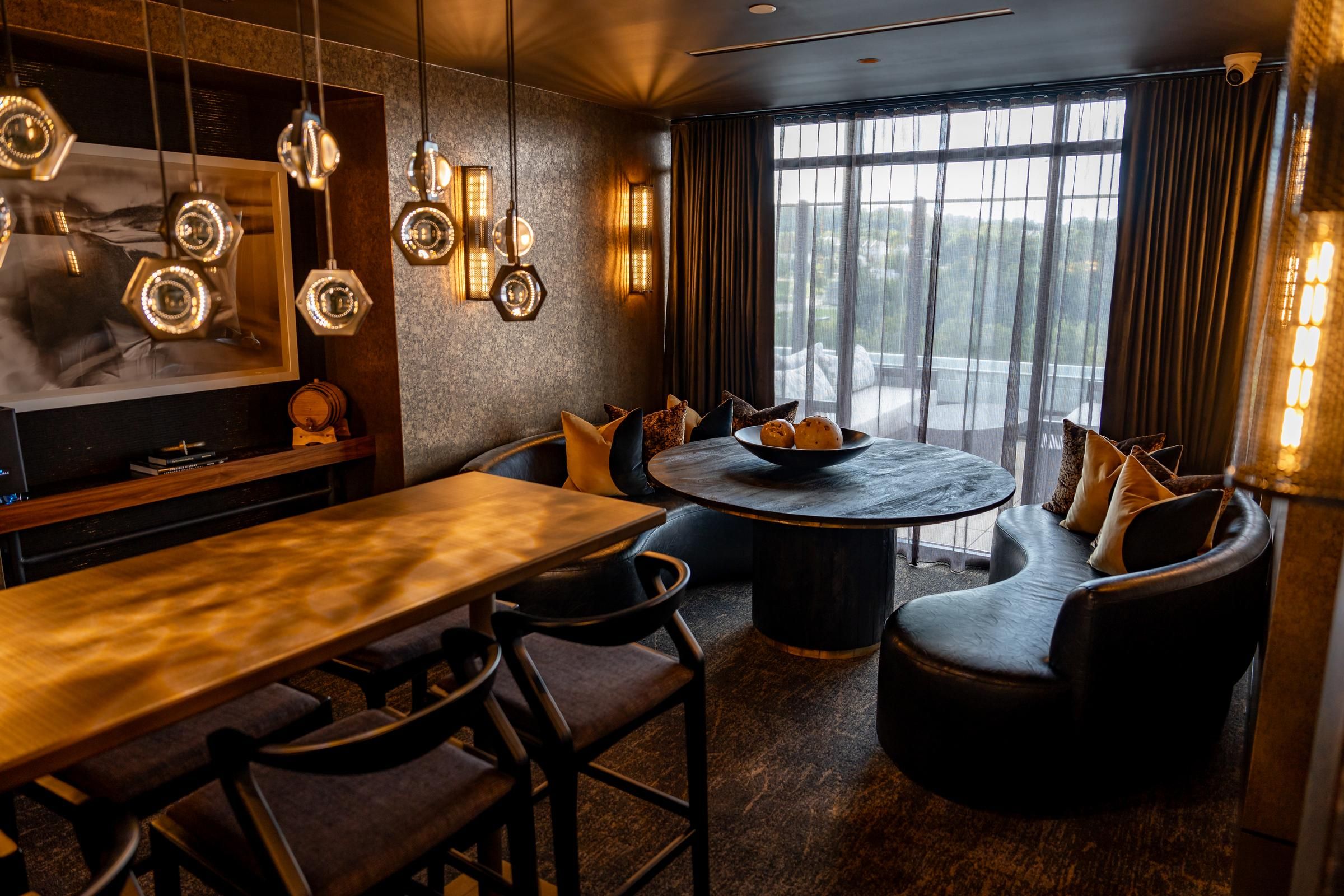 Madison West Elm apartments Modern lounge with a wooden table, pendant lights, curved sofa, and large windows with sheer curtains.