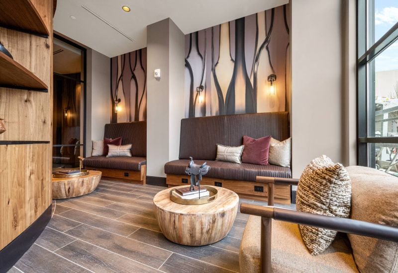 Madison West Elm apartments Modern lounge with wood accents, built-in seating, round tables, and abstract wall art in natural tones.