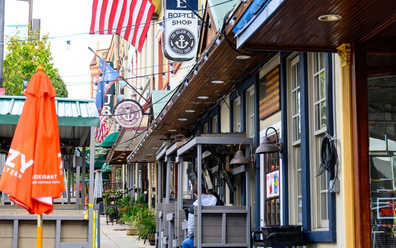 Colorful sidewalk with outdoor seating, American flag, and barber shop sign along a row of shops in Conshohocken, PA near Madison West Elm apartments.