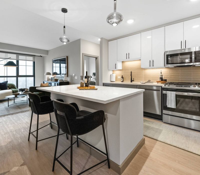 Madison West Elm apartments Modern kitchen with white cabinets, island seating, and stainless steel appliances, open to a living area.
