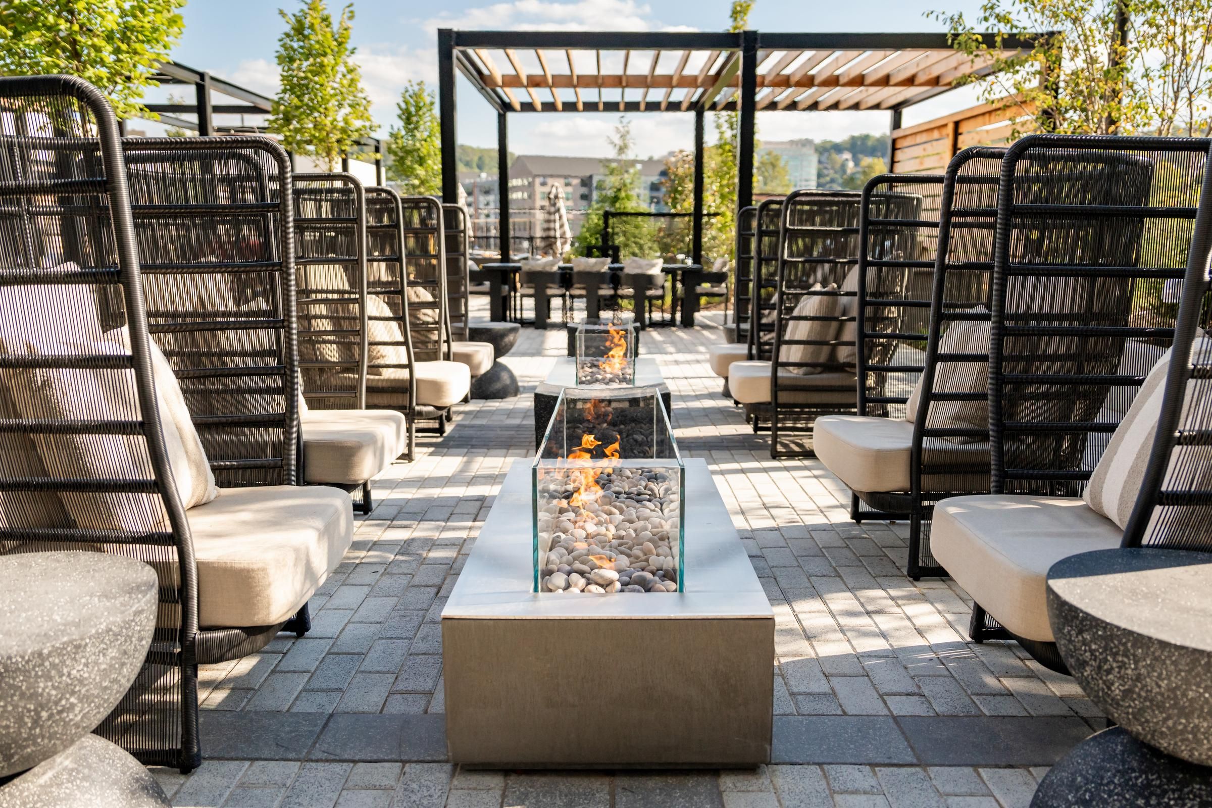 Madison West Elm apartments Modern outdoor patio with cushioned seating, glass fire pits, and a wooden pergola under a sunny sky.