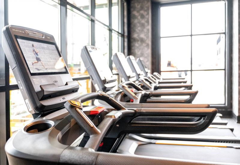 Madison West Elm apartments Row of modern treadmills in a brightly lit gym, each with a screen displaying a running video.