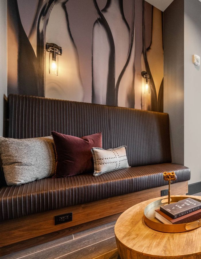 Madison West Elm apartments Modern lounge with cushioned benches, wood tables, and large window with a city view.