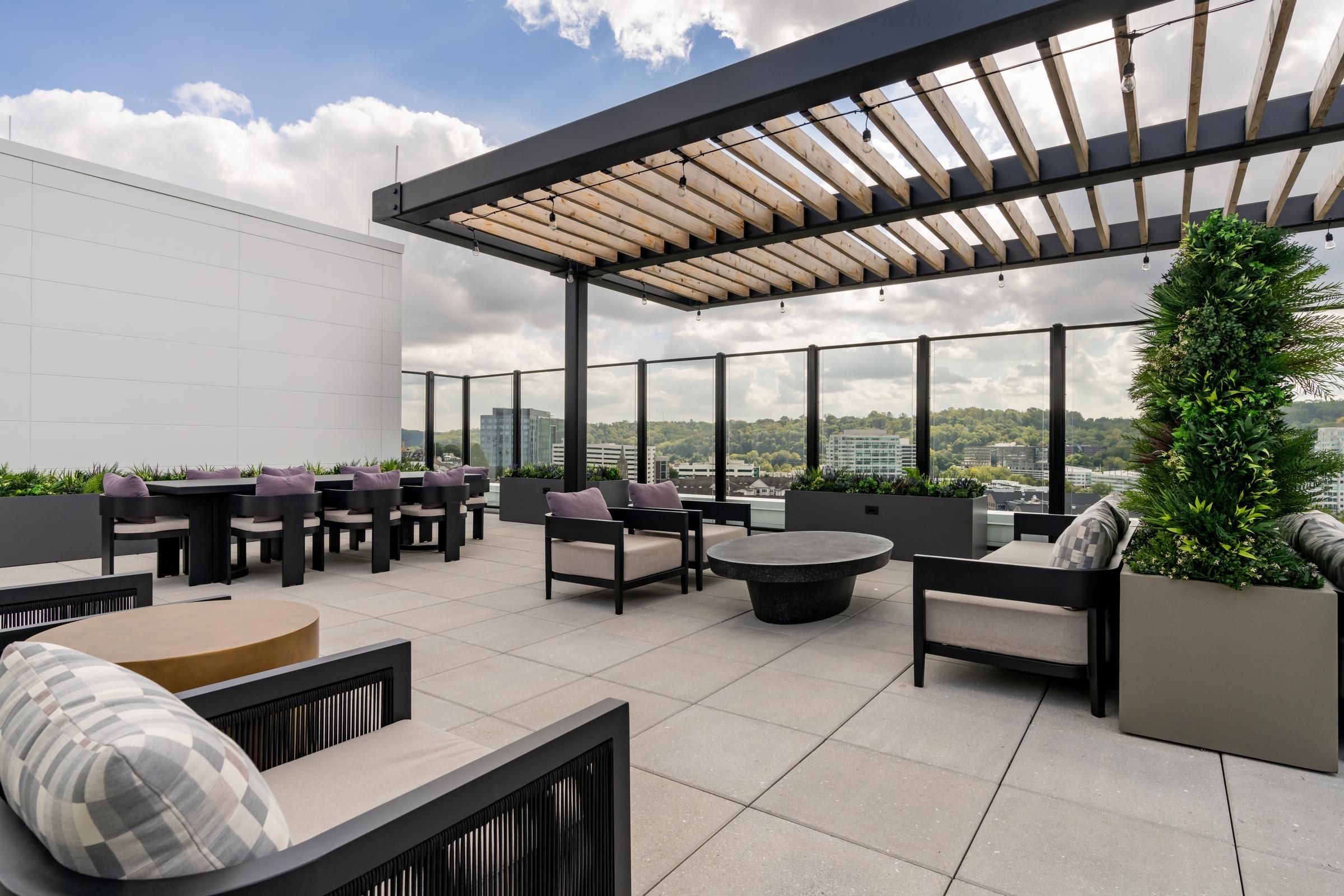 Madison West Elm apartments Modern rooftop patio with lounge chairs, tables, pergola, and city views under a partly cloudy sky.