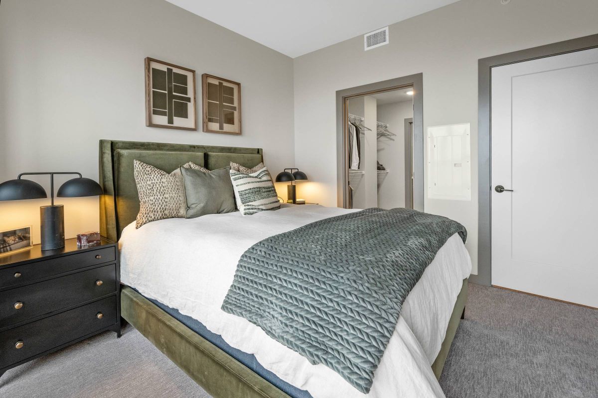 Madison West Elm apartments Modern bedroom with green accents, two nightstands, lamps, and framed art above the bed.