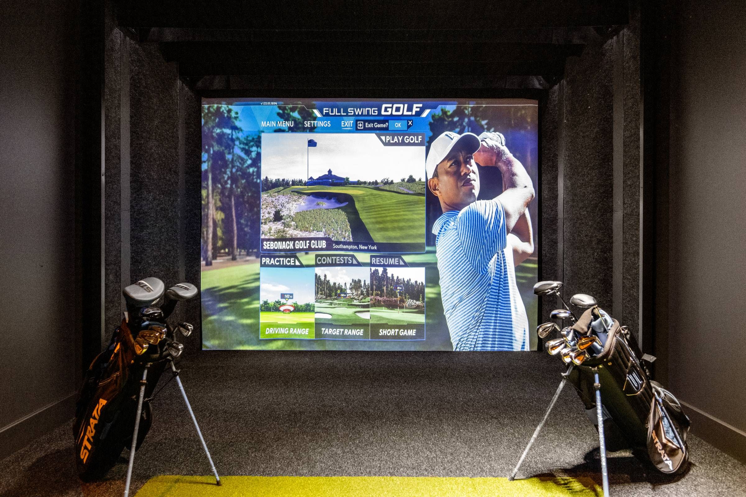 Madison West Elm apartments Indoor golf simulator setup with two golf bags and a virtual golf course displayed on a large screen.