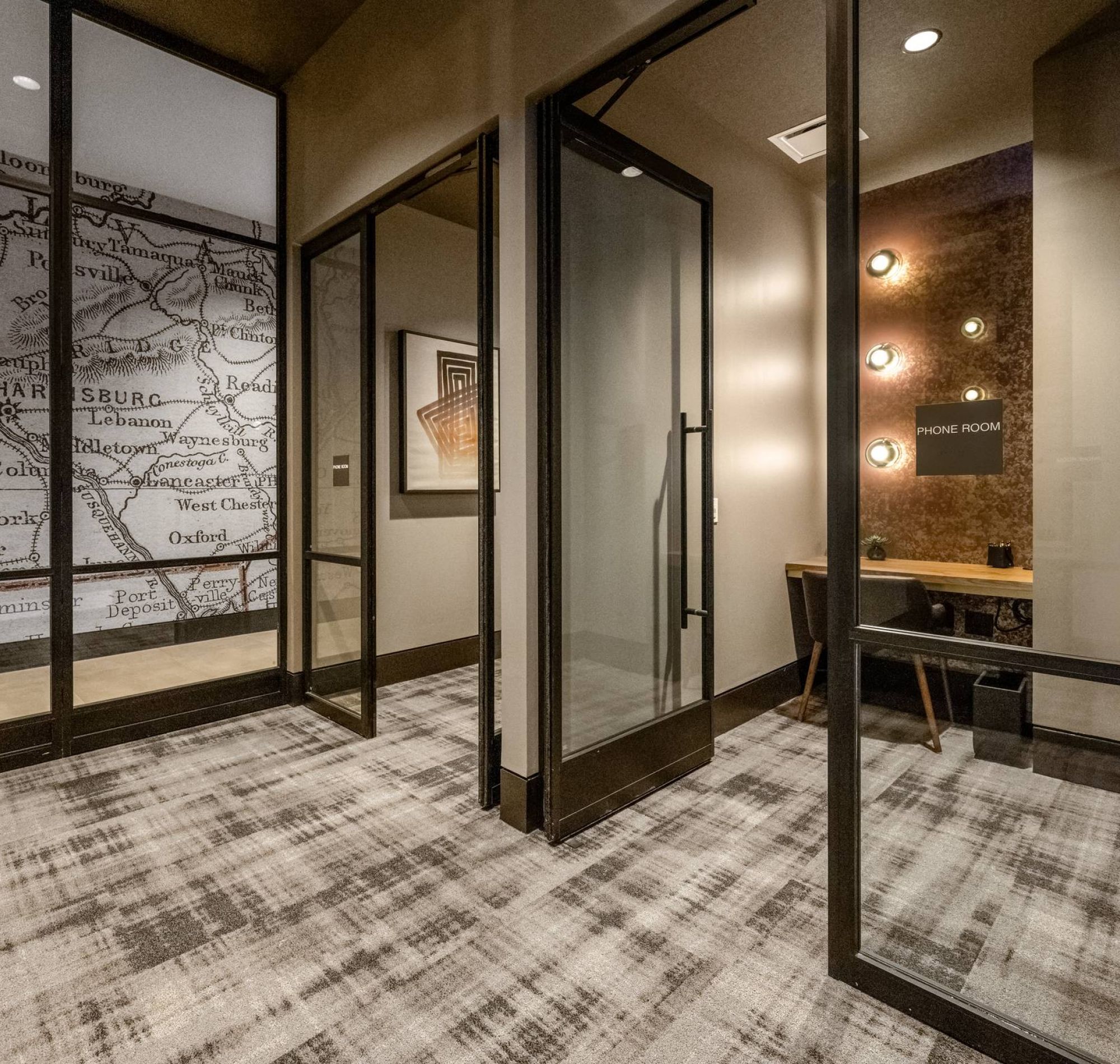Madison West Elm apartments Modern office space with glass walls, a map mural, and a small phone room with a desk and wall lights.