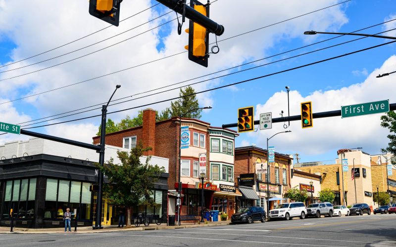 A busy street intersection with shops, traffic lights, parked cars, and people on the sidewalk in  Conshohocken, PA near Madison West Elm apartments.