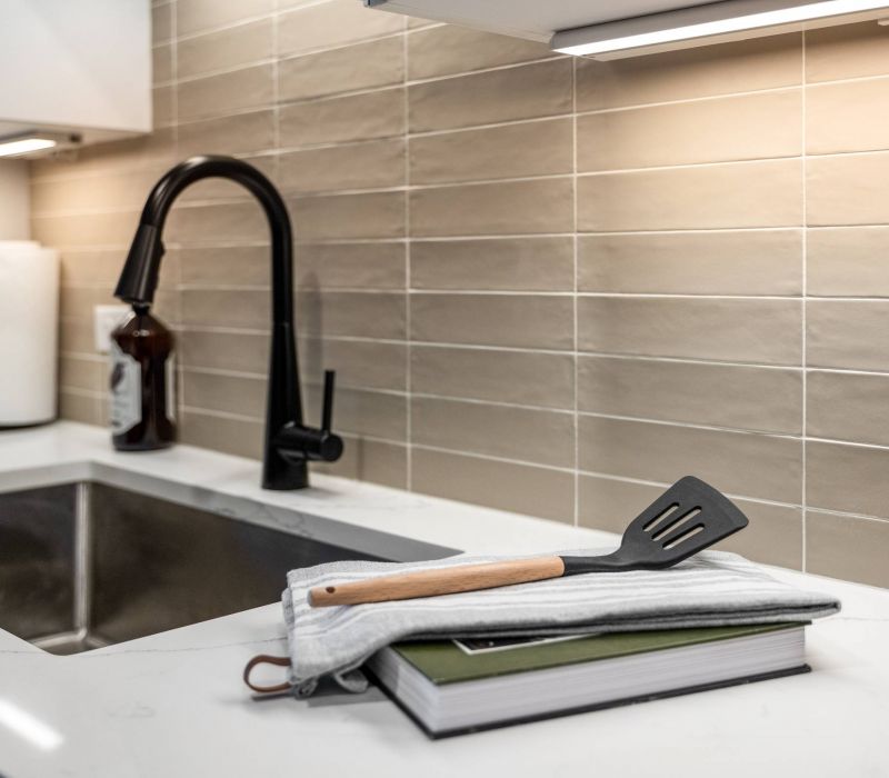 Madison West Elm apartments A spatula rests on a folded towel and book beside a kitchen sink with a black faucet.