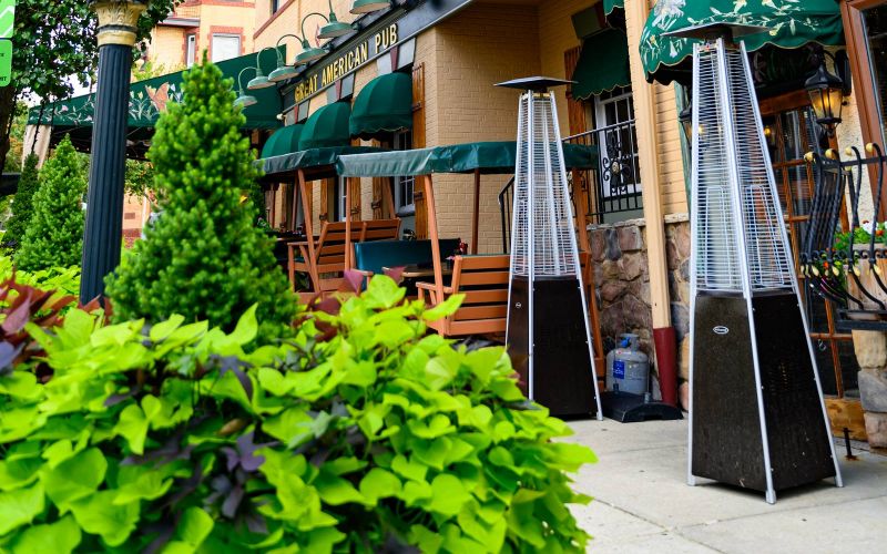 Outdoor view of Great American Pub with green awnings, two American flags, and a vintage street clock in Conshohocken, PA near Madison West Elm apartments.
