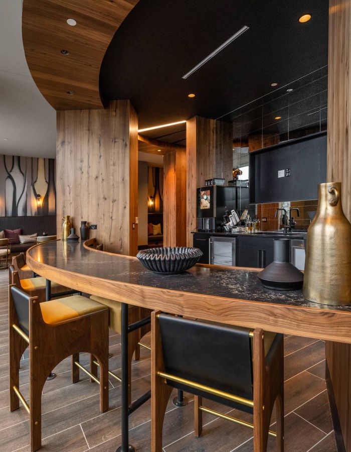 Madison West Elm apartments Modern lounge with wood accents, curved table, tall windows, and a sleek open kitchen in the background.