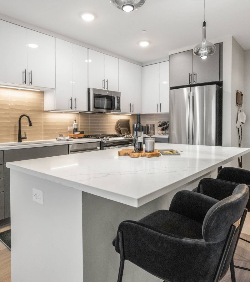 Madison West Elm apartments Modern kitchen with white cabinets, stainless steel appliances, and a marble island with two black chairs.