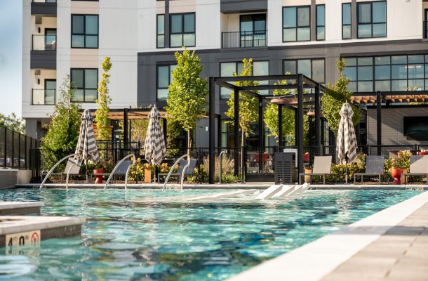 Madison West Elm apartments Modern apartment building with a pool, lounge chairs, umbrellas, and green plants on a sunny day.
