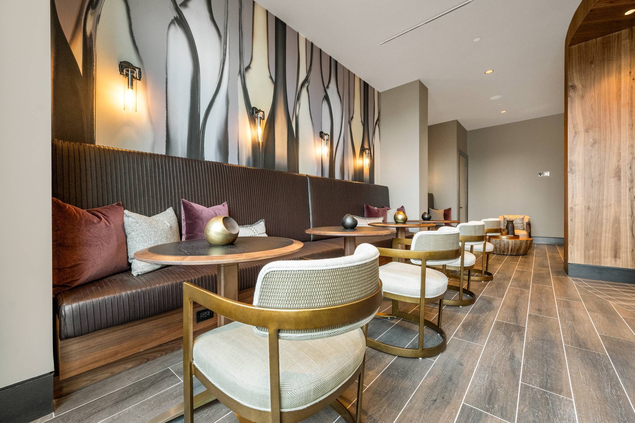 Madison West Elm apartments Modern lounge with booth seating, round tables, stylish chairs, wood flooring, and abstract wall art.