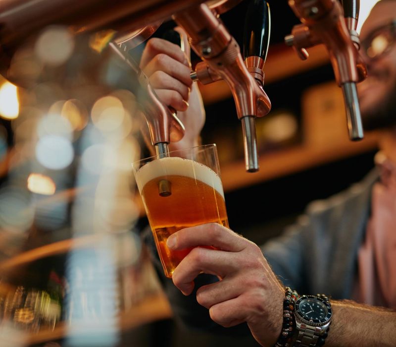 Bartender pouring a draft beer into a glass from a tap at a bar, with foam forming on top.