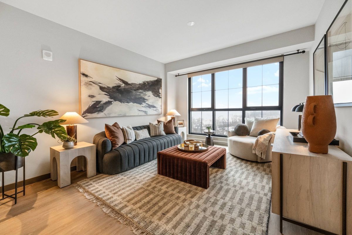 Madison West Elm apartments Modern living room with large window, cozy seating, neutral décor, plants, and abstract artwork on the wall.
