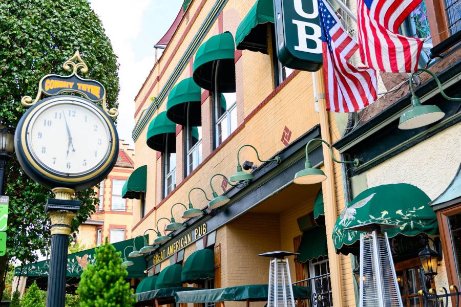 Outdoor view of Great American Pub with green awnings, two American flags, and a vintage street clock in Conshohocken, PA near Madison West Elm apartments.