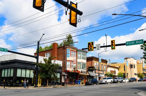 A busy street intersection with shops, traffic lights, parked cars, and people on the sidewalk in Conshohocken, PA near Madison West Elm apartments.