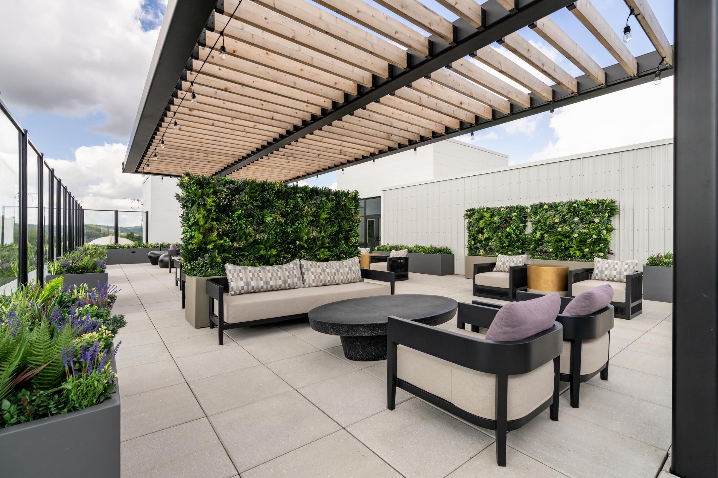 Madison West Elm apartments Modern rooftop patio with lounge seating, greenery walls, and a wooden pergola under a partly cloudy sky.