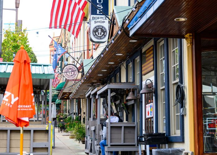 Colorful sidewalk with outdoor seating, American flag, and barber shop sign along a row of shops in Conshohocken, PA near Madison West Elm apartments.