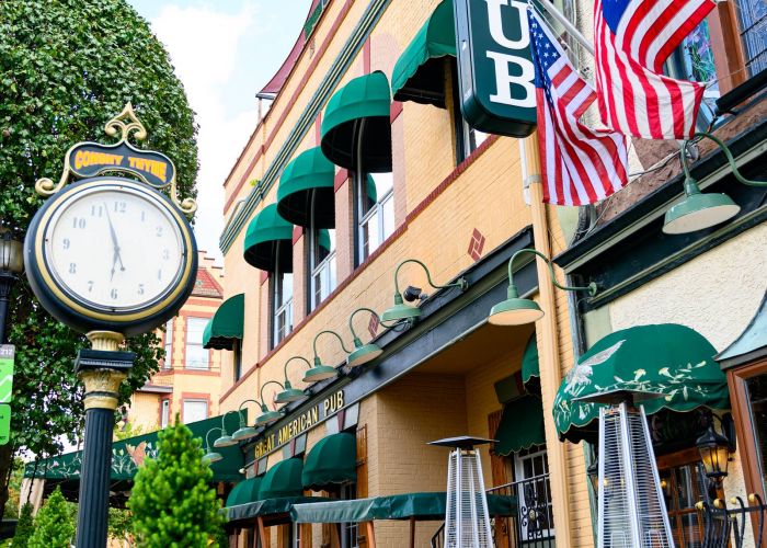 Outdoor view of Great American Pub with green awnings, two American flags, and a vintage street clock in Conshohocken, PA near Madison West Elm apartments.