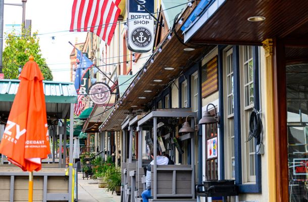 Colorful sidewalk with outdoor seating, American flag, and barber shop sign along a row of shops in Conshohocken, PA near Madison West Elm apartments.